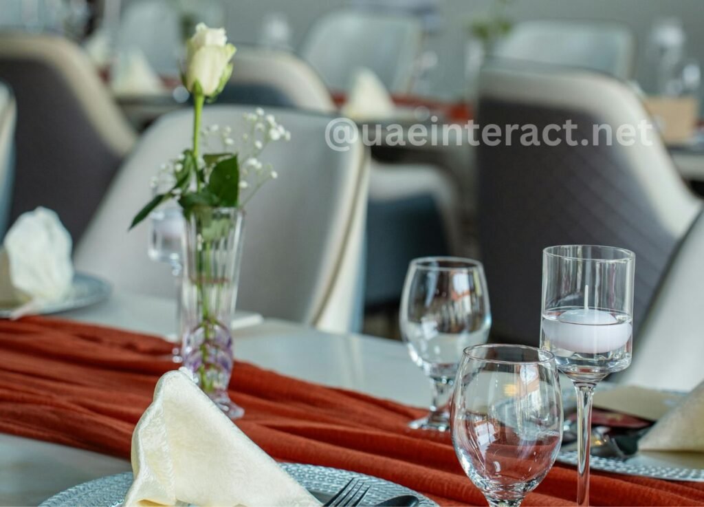 Elegant table setting with a white rose centerpiece in a glass vase, crystal glasses, and a red table runner.