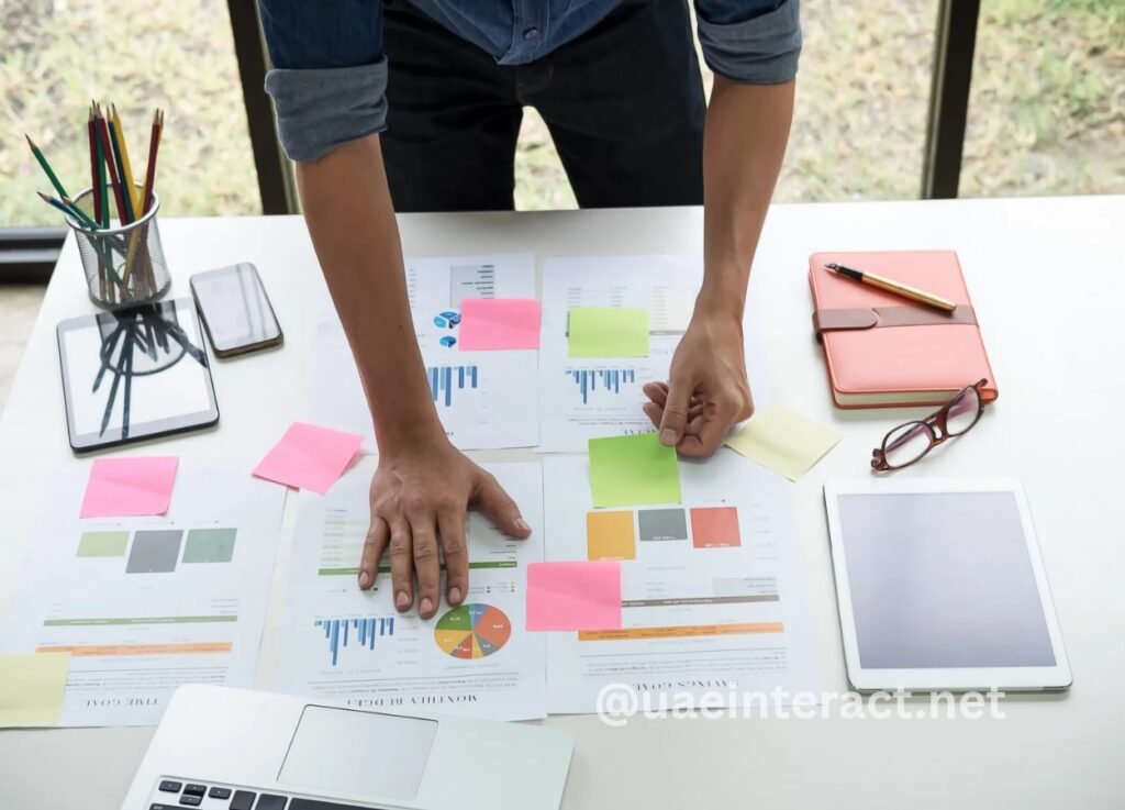 Person arranges colorful charts and sticky notes on a desk during a brainstorming session.
