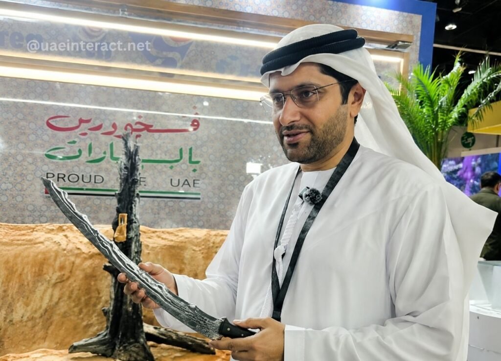 Man in traditional Emirati attire holding a curved ceremonial dagger at a UAE exhibition booth with 'Proud to be UAE' signage in the background.