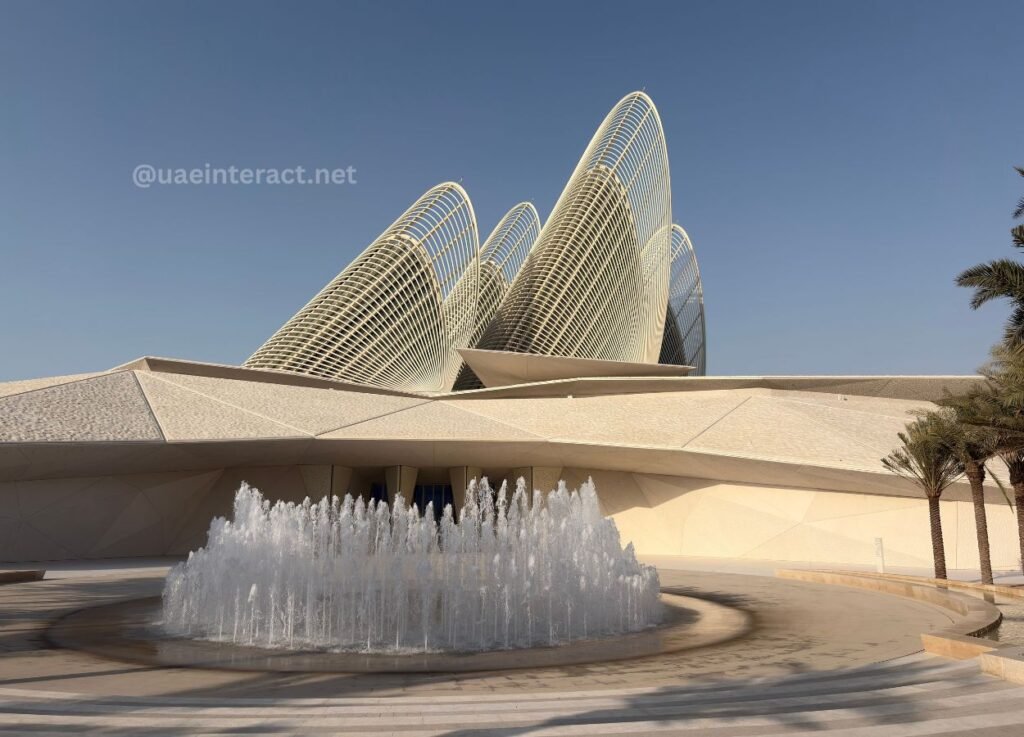 Abu Dhabi Strengthens Global Standing Through Landmark Cultural and Tourism Projects - UAE Interact Circular fountain with jets in front of a futuristic beige building featuring curved white lattice arches against a clear blue sky.